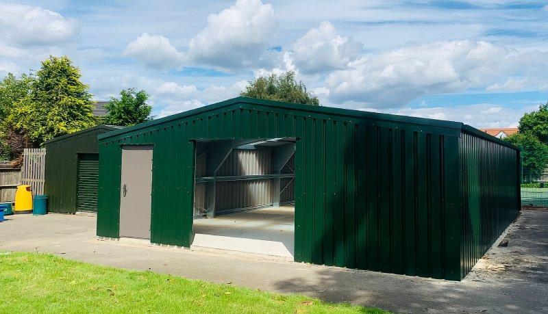 Front exterior of a dark green steel building with an open central bay revealing the internal structure.